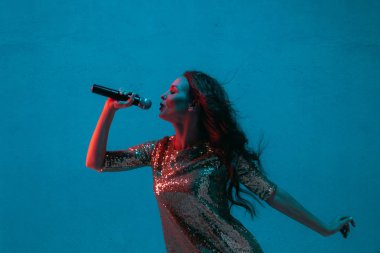 Caucasian female singer portrait isolated on blue studio background in neon light