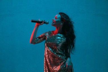 Caucasian female singer portrait isolated on blue studio background in neon light
