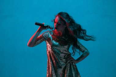 Caucasian female singer portrait isolated on blue studio background in neon light