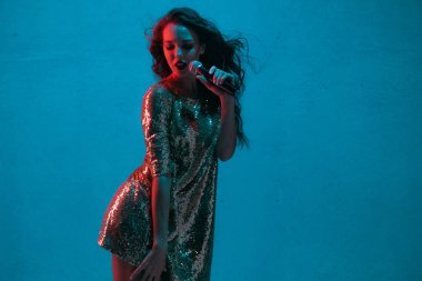Caucasian female singer portrait isolated on blue studio background in neon light