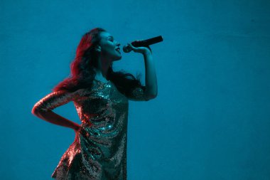 Caucasian female singer portrait isolated on blue studio background in neon light