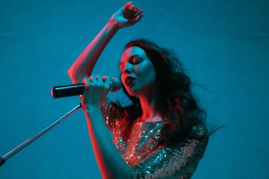 Caucasian female singer portrait isolated on blue studio background in neon light