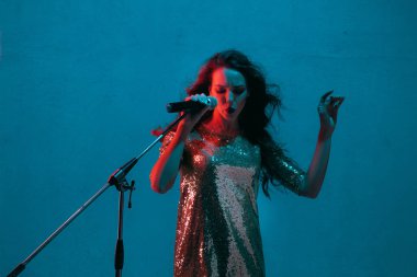 Caucasian female singer portrait isolated on blue studio background in neon light