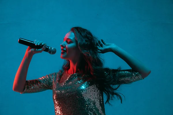 Retrato femenino de cantante caucásica aislado sobre fondo estudio azul en luz de neón —  Fotos de Stock