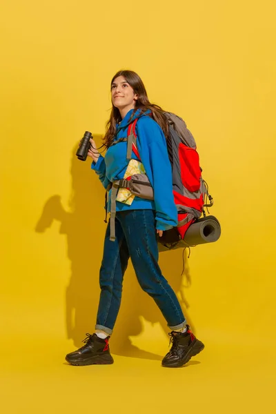 Full length portrait of a cheerful young caucasian tourist girl isolated on yellow background — Stock Photo, Image