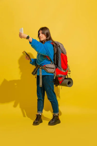 Full length portrait of a cheerful young caucasian tourist girl isolated on yellow background — Stock Photo, Image