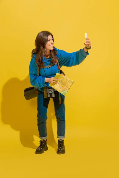 Full length portrait of a cheerful young caucasian tourist girl isolated on yellow background — Stock Photo, Image