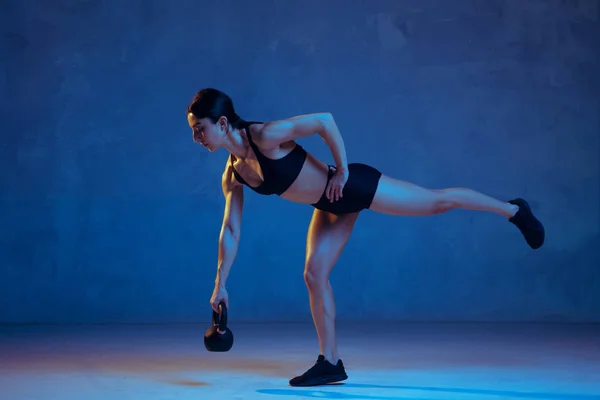 Caucasian young female athlete practicing on blue studio background in neon light — Stock Photo, Image