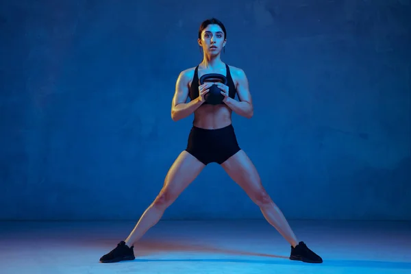 Giovane atleta caucasica femminile che pratica su sfondo blu studio in luce al neon — Foto Stock