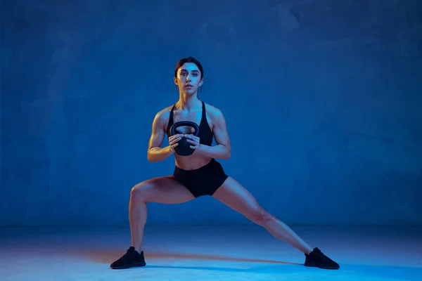 Кавказская юная спортсменка практикуется на голубом студийном фоне в неоновом свете — стоковое фото