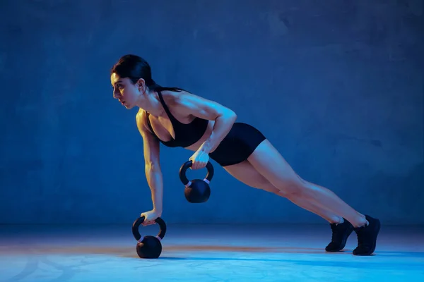 Branco jovem atleta do sexo feminino praticando em fundo estúdio azul em luz de néon — Fotografia de Stock