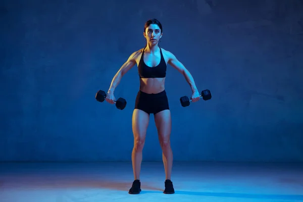 Beyaz tenli genç bayan atlet mavi stüdyo arka planında neon ışıklarıyla pratik yapıyor. — Stok fotoğraf