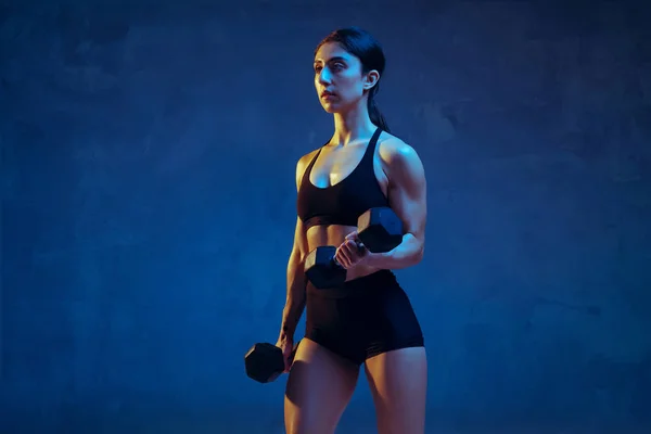 Kaukasische jonge vrouwelijke atleet oefenen op blauwe studio achtergrond in neon licht — Stockfoto