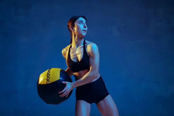 Branco jovem atleta do sexo feminino praticando em fundo estúdio azul em luz de néon — Fotografia de Stock