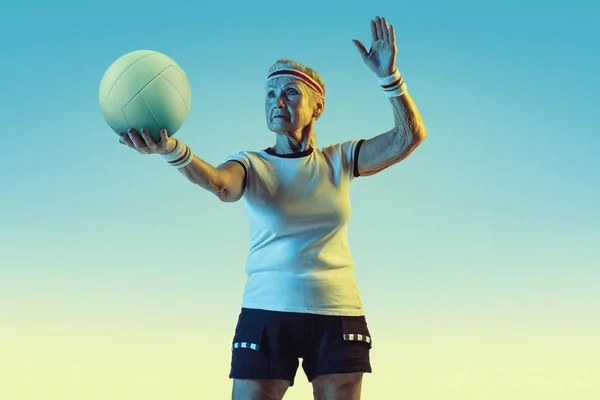 Seniorin beim Volleyballtraining in Sportbekleidung auf Steigungshintergrund in Neonlicht — Stockfoto