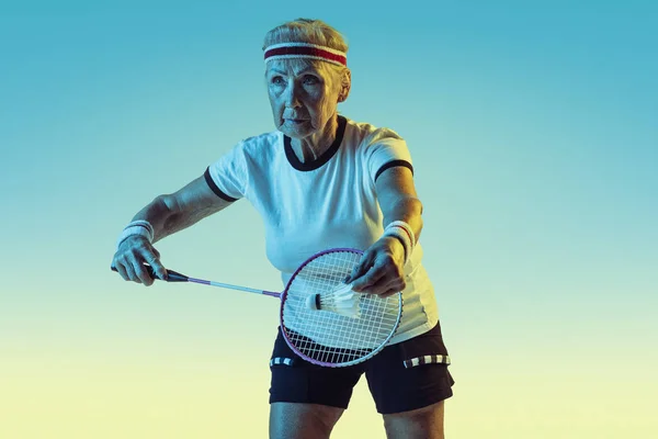 Femme âgée jouant au badminton en tenue de sport sur fond dégradé au néon — Photo