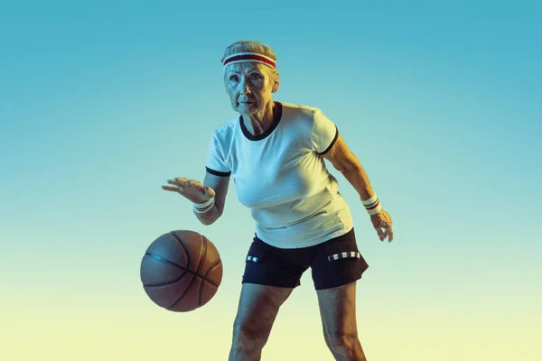 Senior vrouw basketbal spelen in sportschoeisel op gradiënt achtergrond in neon licht — Stockfoto
