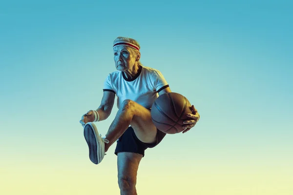 Seniorin spielt Basketball in Sportbekleidung auf Gradienten Hintergrund in Neonlicht — Stockfoto