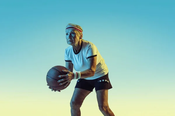Seniorin spielt Basketball in Sportbekleidung auf Gradienten Hintergrund in Neonlicht — Stockfoto