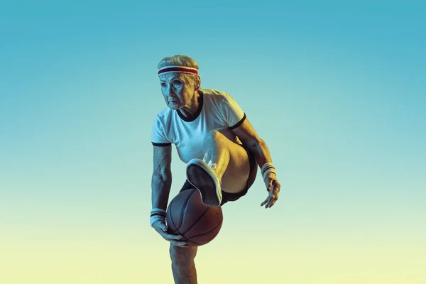 Старша жінка грає в баскетбол у спортивному одязі на градієнтному фоні в неоновому світлі — стокове фото