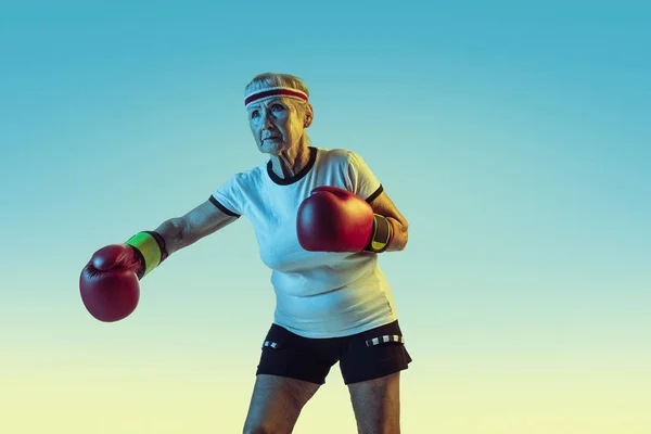 Mulher sênior boxe em sportwear no fundo gradiente em luz de néon — Fotografia de Stock