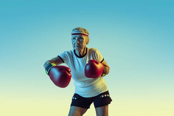 Mulher sênior boxe em sportwear no fundo gradiente em luz de néon — Fotografia de Stock