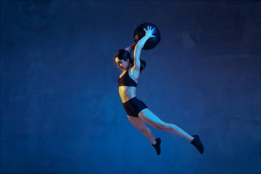 Beyaz tenli genç bayan atlet mavi stüdyo arka planında neon ışıklarıyla pratik yapıyor.