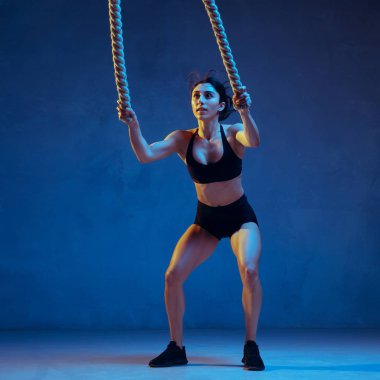 Beyaz tenli genç bayan atlet mavi stüdyo arka planında neon ışıklarıyla pratik yapıyor.