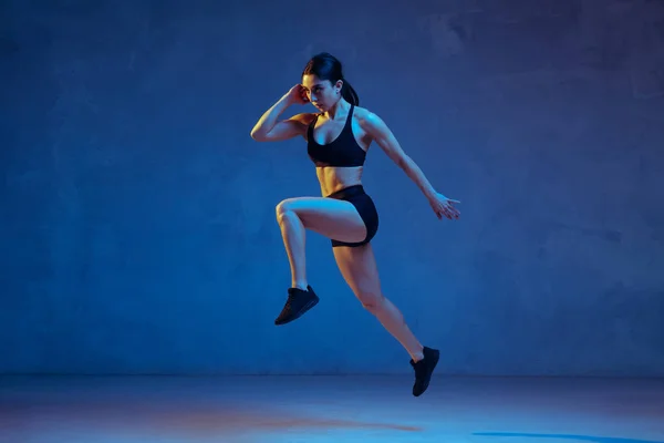Caucasian young female athlete practicing on blue studio background in neon light