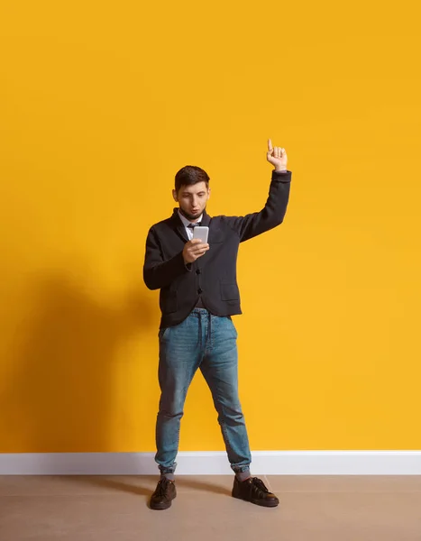 Joven hombre caucásico usando smartphone. Retrato de cuerpo entero aislado sobre fondo amarillo . — Foto de Stock