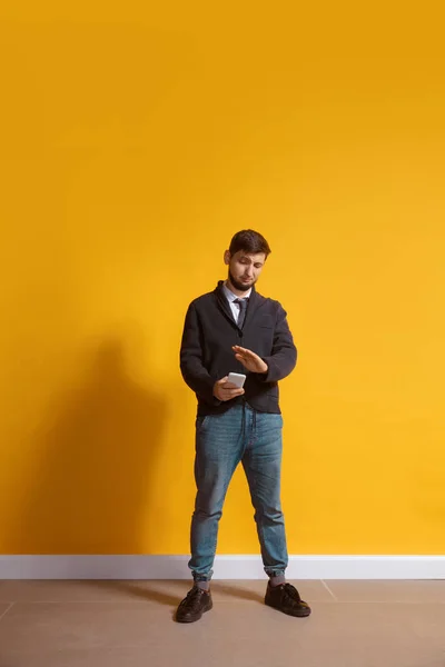 Giovane uomo caucasico utilizzando smartphone. Lunghezza del corpo intero ritratto isolato su sfondo giallo . — Foto Stock