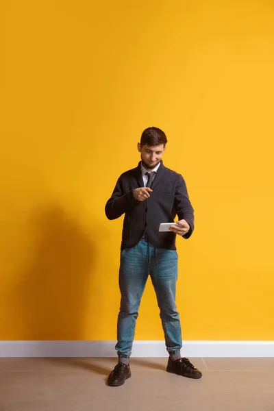 Joven hombre caucásico usando smartphone. Retrato de cuerpo entero aislado sobre fondo amarillo . — Foto de Stock