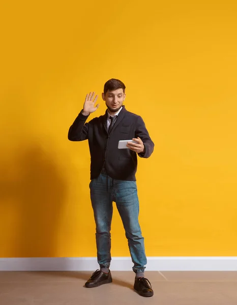 Joven hombre caucásico usando smartphone. Retrato de cuerpo entero aislado sobre fondo amarillo . — Foto de Stock