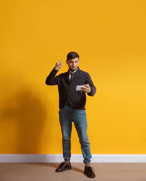 Joven hombre caucásico usando smartphone. Retrato de cuerpo entero aislado sobre fondo amarillo . — Foto de Stock