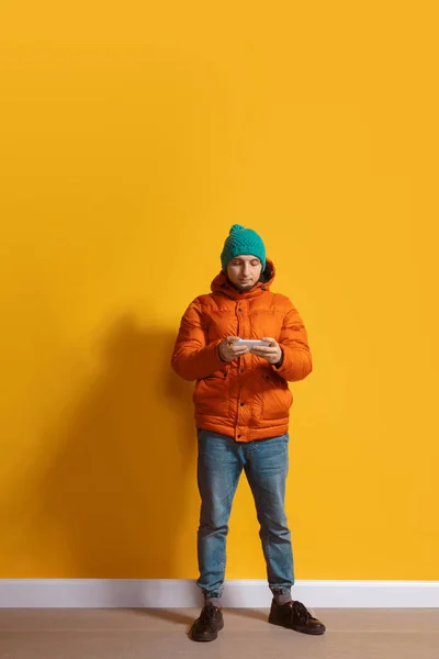 Joven hombre caucásico usando smartphone. Retrato de cuerpo entero aislado sobre fondo amarillo . — Foto de Stock