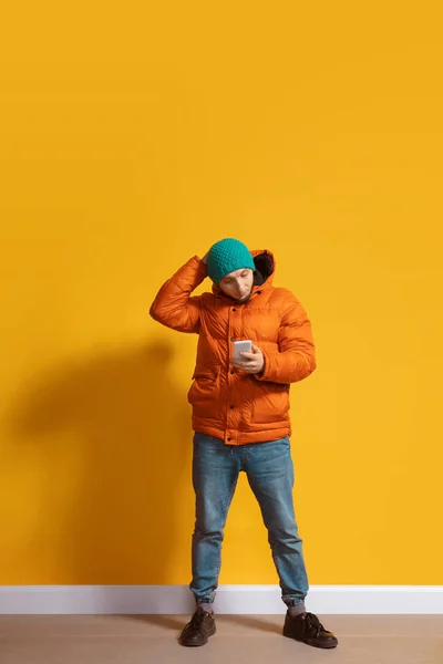 Joven hombre caucásico usando smartphone. Retrato de cuerpo entero aislado sobre fondo amarillo . — Foto de Stock