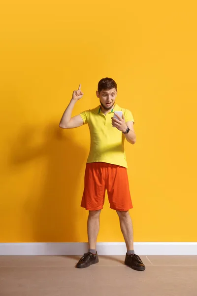 Joven hombre caucásico usando smartphone. Retrato de cuerpo entero aislado sobre fondo amarillo . — Foto de Stock