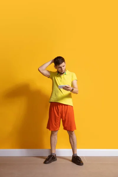 Een jonge blanke man die een smartphone gebruikt. Volledige lichaamslengte portret geïsoleerd over gele achtergrond. — Stockfoto