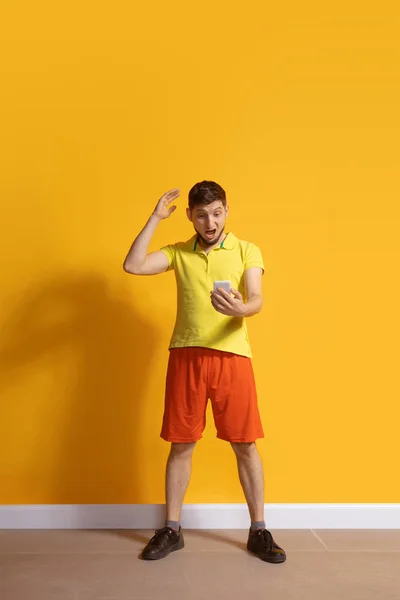 Joven hombre caucásico usando smartphone. Retrato de cuerpo entero aislado sobre fondo amarillo . — Foto de Stock