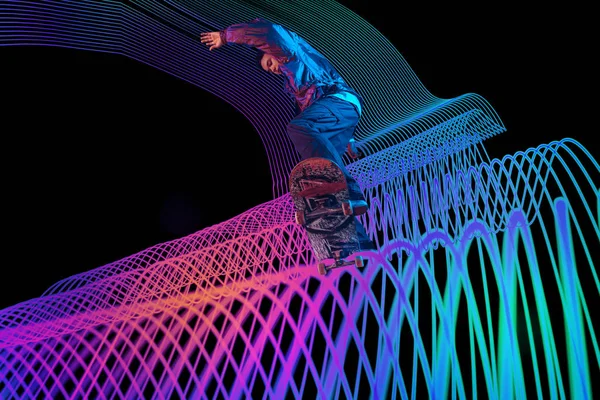 Kaukasische jonge skateboarder rijden op donkere neon verlichte lijn achtergrond — Stockfoto