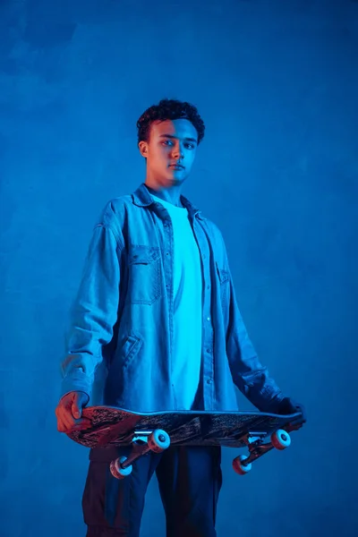 Vit ung skateboardåkare poserar på mörk neon belyst bakgrund — Stockfoto