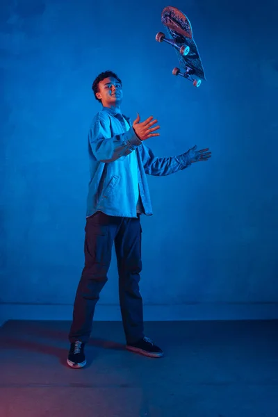 Caucásico joven skateboarder posando sobre oscuro neón iluminado fondo —  Fotos de Stock