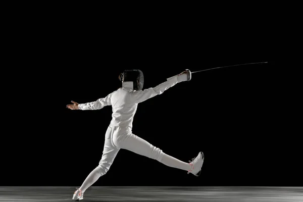 Teen girl in fencing costume with sword in hand isolated on black background