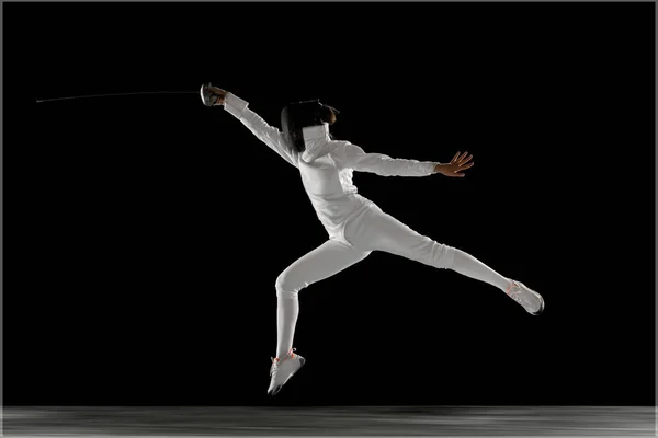 Adolescente en costume d'escrime avec épée à la main isolé sur fond noir — Photo