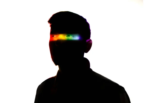 Dramatiskt porträtt av en man i mörkret på vit studio bakgrund med regnbåge färgade linje — Stockfoto