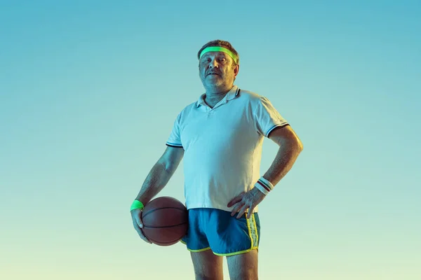 Hombre mayor jugando baloncesto en ropa deportiva sobre fondo degradado y luz de neón — Foto de Stock