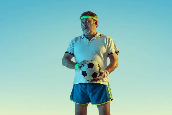 Hombre mayor jugando fútbol en ropa deportiva sobre fondo degradado y luz de neón — Foto de Stock