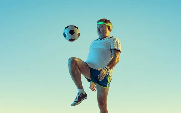 Uomo anziano che gioca a calcio in abbigliamento sportivo su sfondo sfumato e luce al neon — Foto Stock
