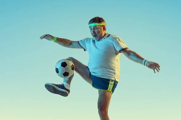 Senior-Mann spielt Fußball in Sportbekleidung auf Gradientenhintergrund und Neonlicht — Stockfoto