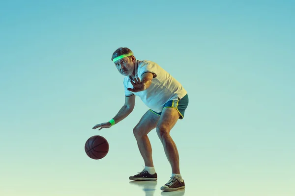 Senior-Mann spielt Basketball in Sportbekleidung auf Gradientenhintergrund und Neonlicht — Stockfoto